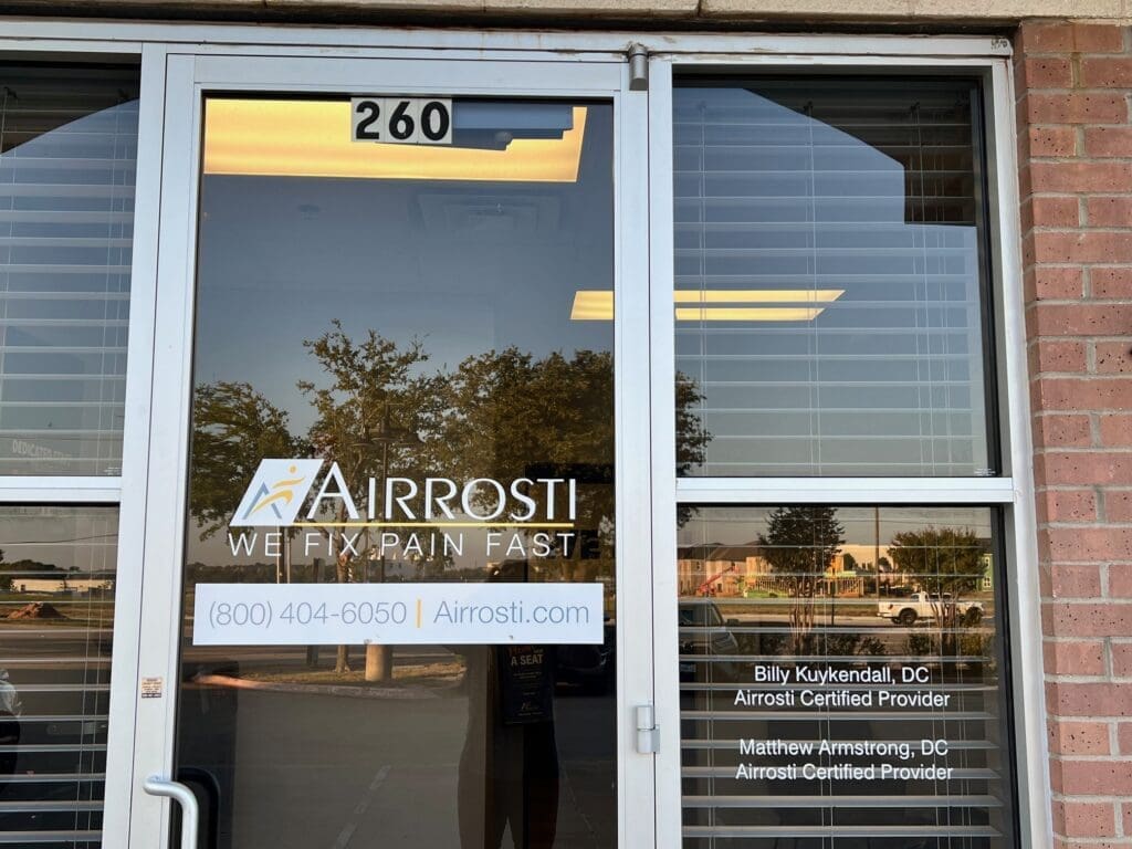 Photo of the exterior entrance of Airrosti Allen. Airrosti logo printed on the glass of the front door
