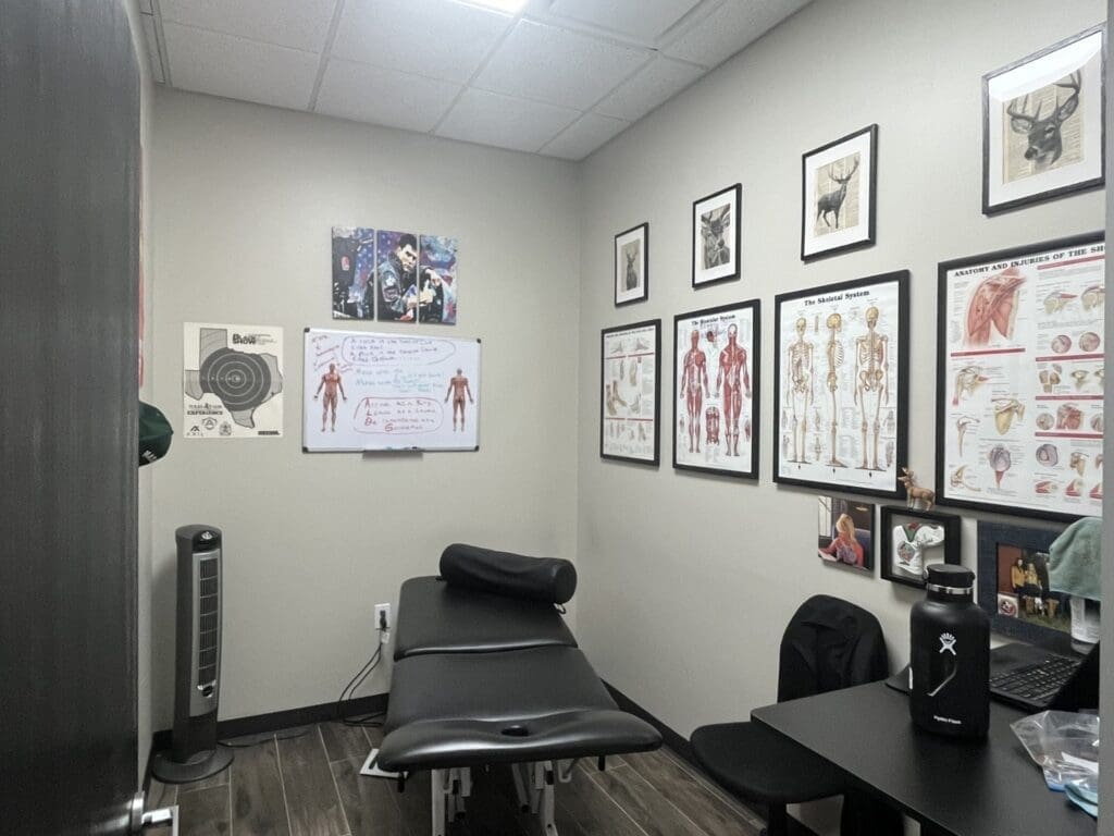 A photo of the treatment room at Airrosti Magnolia. A treatment table is featured in the center of the room and the walls are decorated with posters of MSK diagrams.