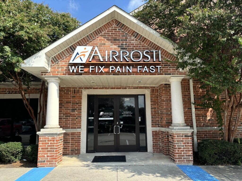 View of exterior entrance at Airrosti McKinney. Airrosti marquis is featured on building.